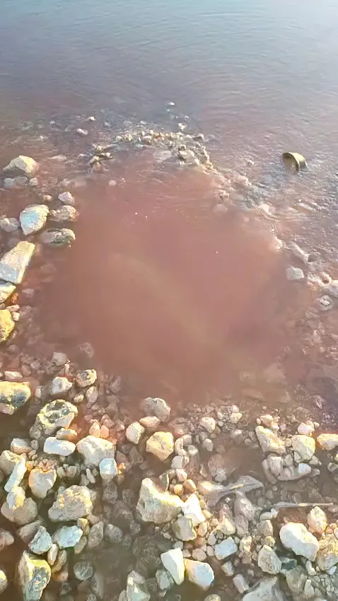 Water pooling over stones and red soil from a leaking pipe on a site
