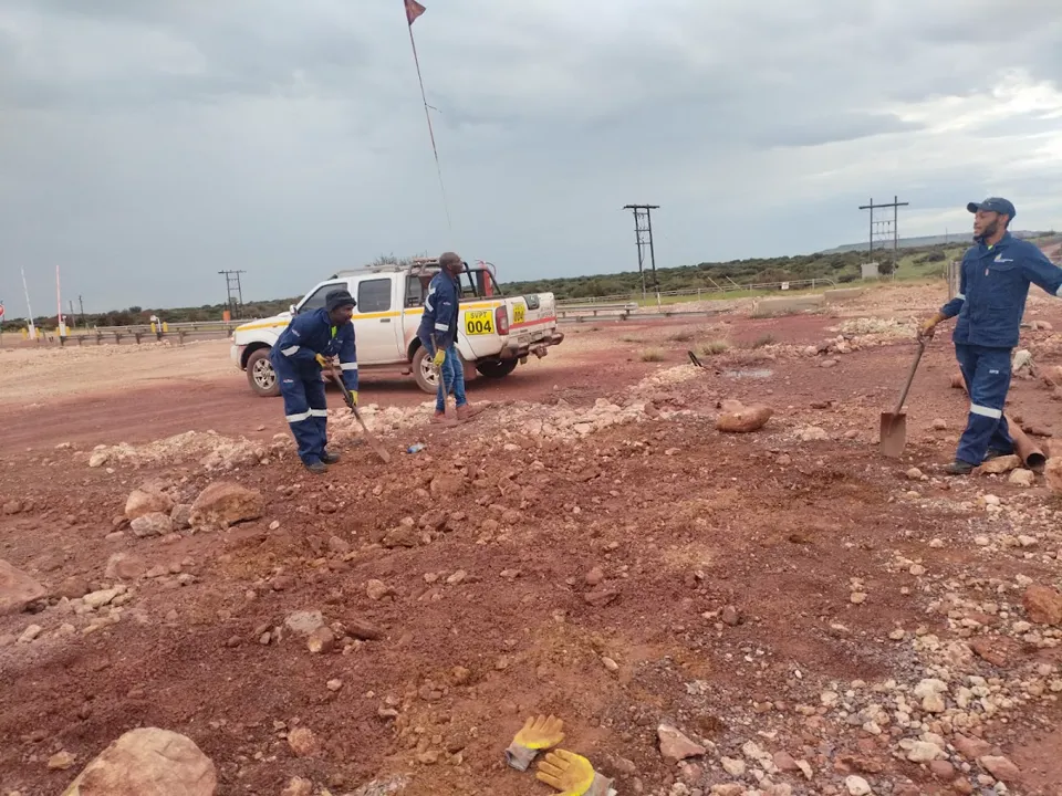 Team with spades on an open red-soil site, a white bakkie behind