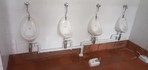 Four new white urinals with new white pipework on a tiled wall